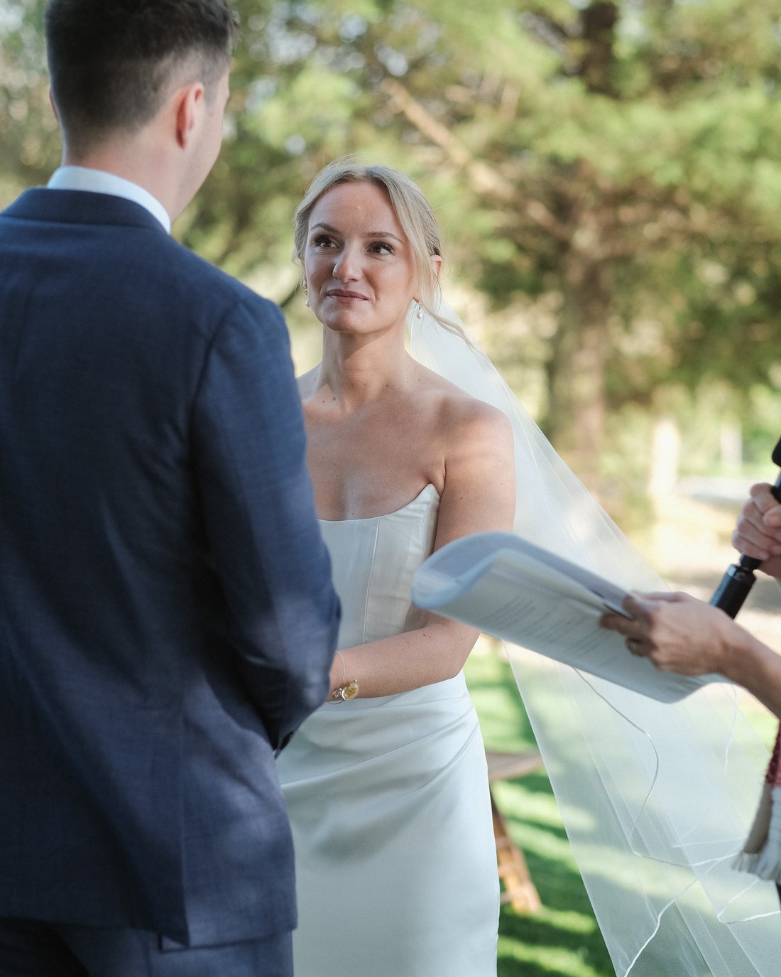 A couple at their ceremony, the bride's veil lifting in the breeze