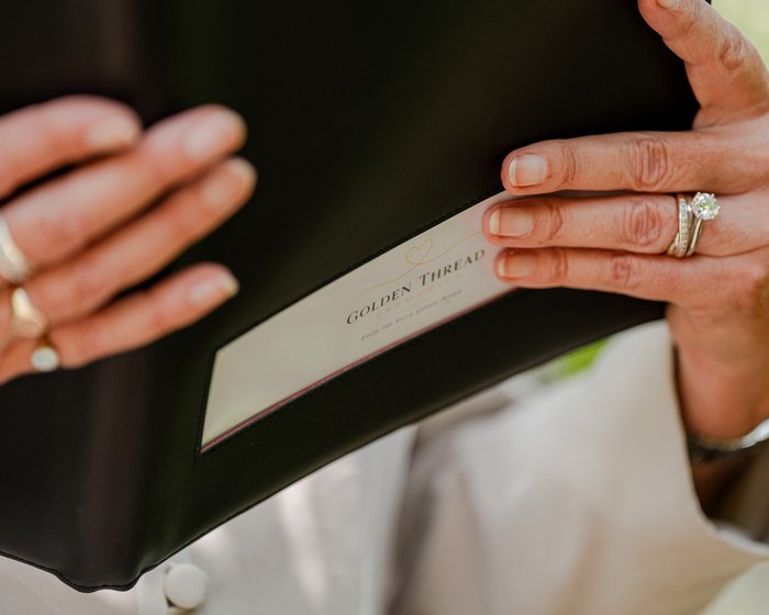 Hands holding an open ceremony card, wedding rings visible