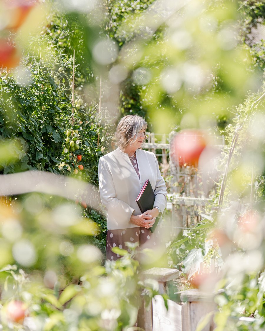 Celebrant Veronica Hale in a sunlit kitchen garden, ceremony folder in hand