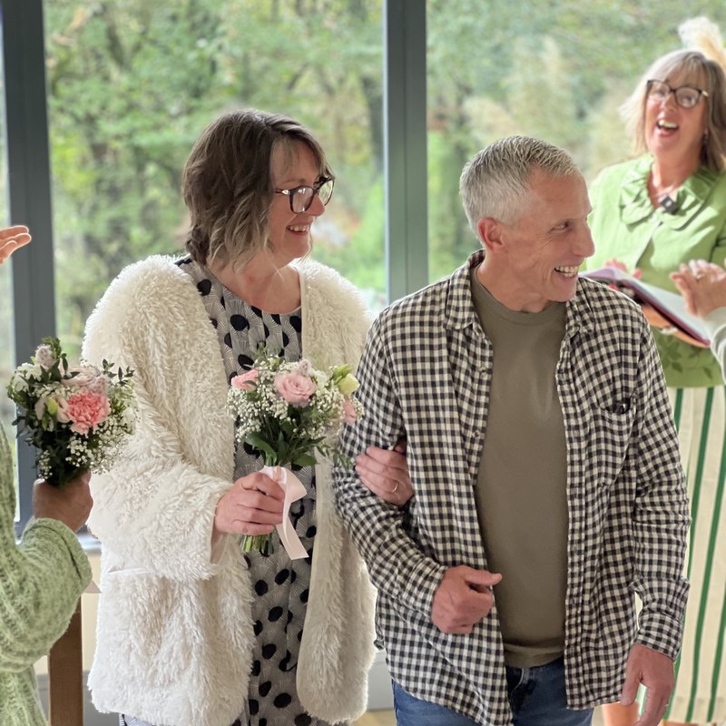 A couple walking arm in arm at their ceremony, celebrant Veronica Hale laughing behind them