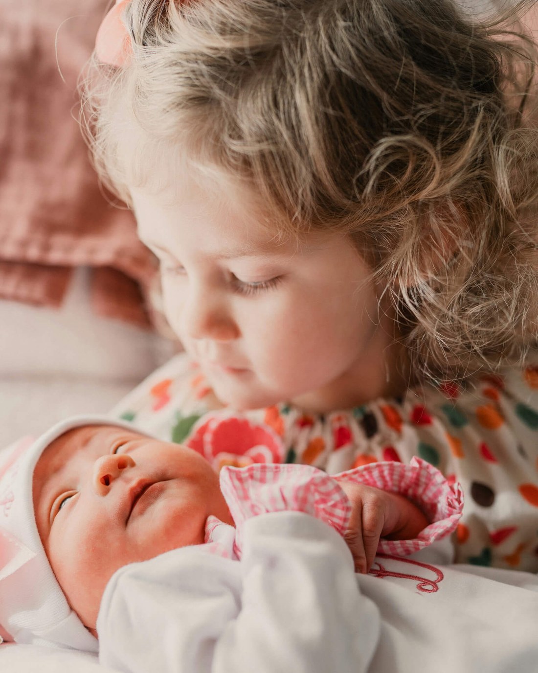 A young child leaning over to look at a newborn baby