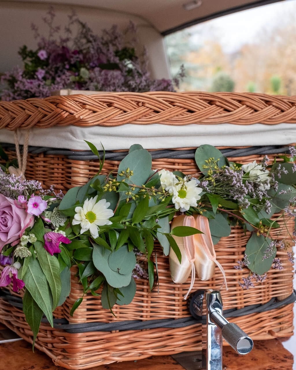 A willow coffin dressed with garden roses and daisies, a pair of ballet slippers laid on top